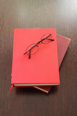 Eyeglasses and two red books laying on wood table
