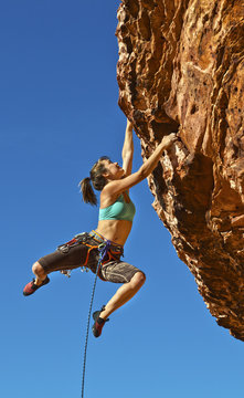 Female rock climber clinging to a cliff.