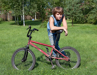 The teenager costs on a solar lawn and leans against a bicycle.