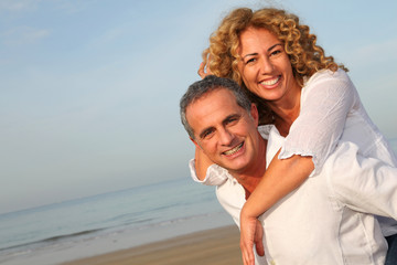 Portrait of happy mature couple at the beach - obrazy, fototapety, plakaty