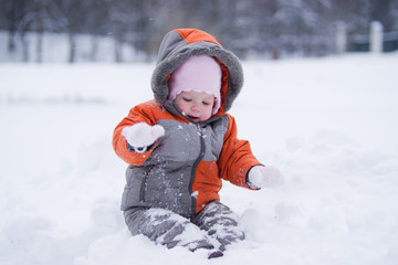 Fototapeta na wymiar cute baby sit on deep fresh snow and dig snow with mittens in p
