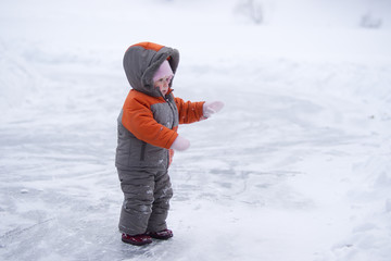 cute wondered baby stay on lake's ice and look to side with hand