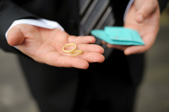 groom holding two gold wedding rings in palm