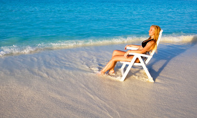 Fototapeta na wymiar Young pretty woman tans in beach chair, it put in ocean..