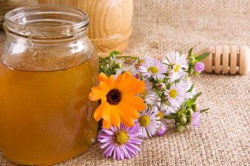 honeycomb, flowers and honey in glass on sack