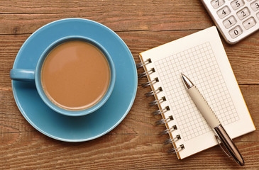 Coffee cup, spiral notebook and pen on the old wooden table