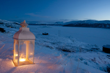 Burning lantern in the snow at dusk