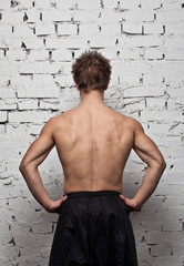 Strong muscular man back at white wall background