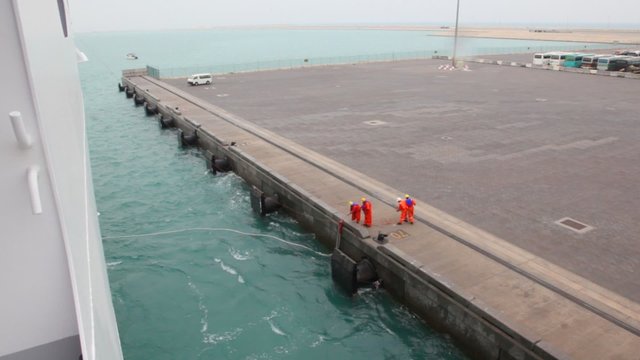 workers ties mooring line of ship to moorage