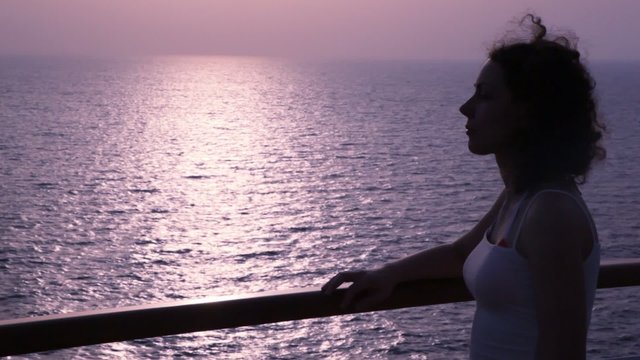 silhouette of woman stands on deck of cruise ship