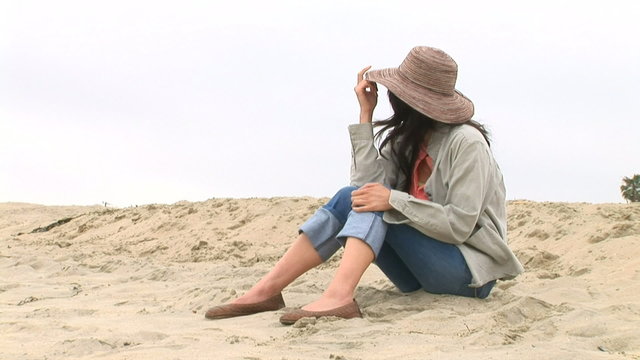 Young woman sitting on sand dunes at beach in cool weather