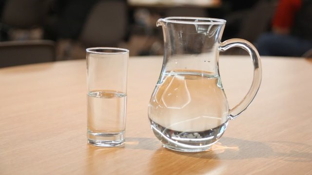 Cup and pitcher filled with water stand on table