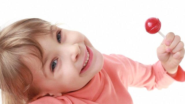 smiling little girl looks at camera and eating lollipop