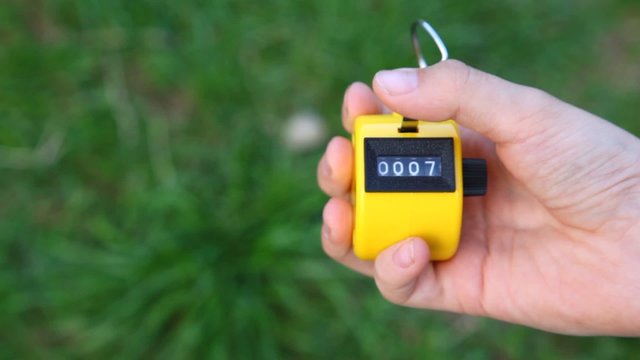 hand of boy using hand-held tally counter against grass