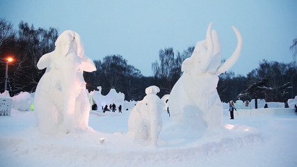 Snow sculptures of mammoths at winter evening on snow town