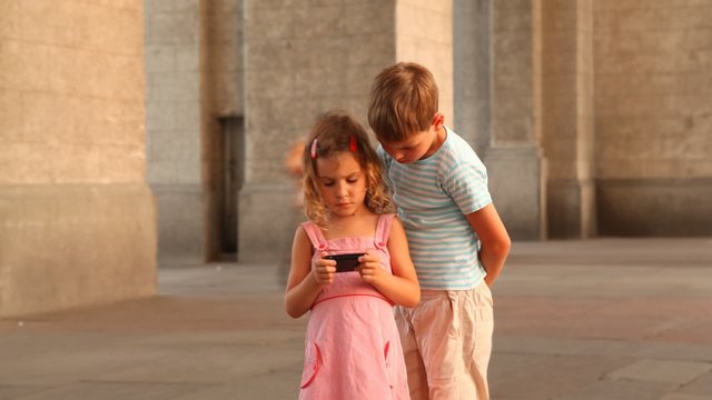 Children are on the square and watching video on smartphone.