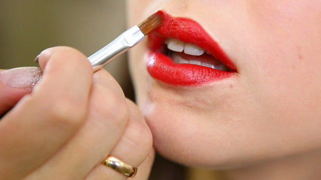 applying bright red lipstick on her lips young girl.