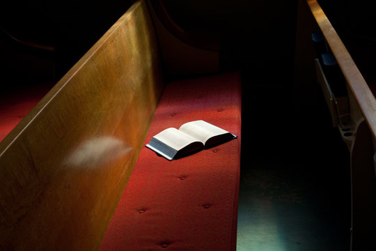 Open Bible Lying on Church Pew in Narrow Sunlight Band