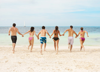 Group of young adults running together on the beach