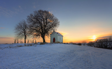 Sunset on frozen field with a chapel and clouds