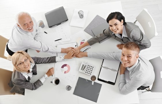 Confident businessteam holding hands at meeting