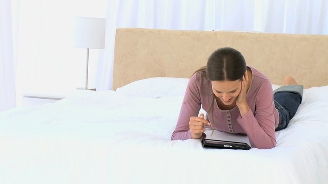 Pretty woman using a computer tablet lying on the bed
