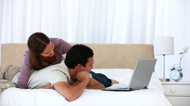 Cute woman hugging her boyfriend while working on laptop