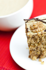 cup of cappuccino, a piece of cake with nuts on a plate lying on