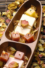 Wooden bowl of soap with rose withered petals on bamboo mat