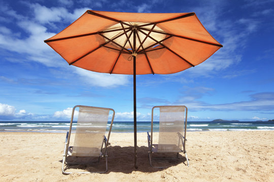 White beach chairs and orange parasol on a tropical beach