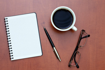 Pen, white spiral notebook and glasses with cup of coffee