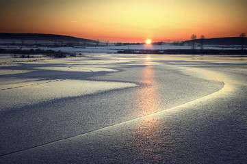 sunset over a frozen lake with a beautiful orange sky