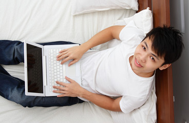 Aerial view of Asian man working with laptop in bed