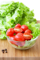 Tomatoes and lettuce in a glass bowl on a wooden chopping board