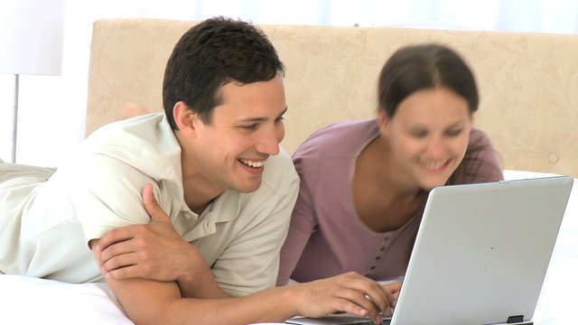 Smiling couple using a laptop lying on the bed