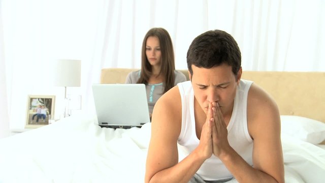 Unhappy man thinking while his wife is working on the laptop