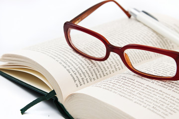 Glasses on book and pen isolated in white