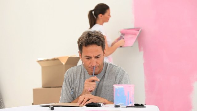 Woman painting a wall while her husband is making a plan