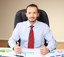 Business man at his workplace hold thumbs up.