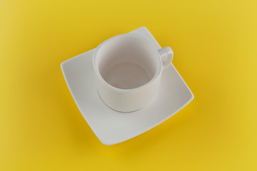 Empty cup with saucer on yellow background.