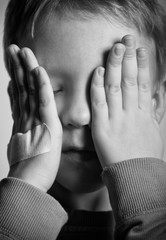 BW portrait of sad crying little boy covers his face with hands