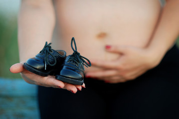 Pregnant girl  and black baby shoes in front of it