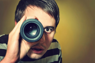 Handsome young man holding camera lens like it was spyglass - obrazy, fototapety, plakaty