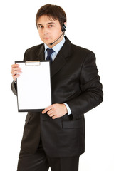 Serious young businessman with headset holding blank clipboard
