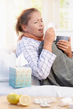 Young woman having flu laying in bed sneezing