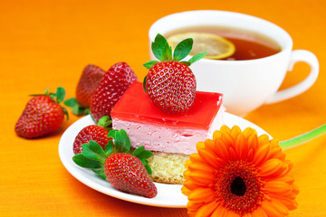 gerbera, lemon tea, cake and strawberries lying on the orange fa