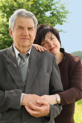 portrait of old senior in suit, his adult daughter leans on his