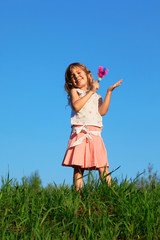 Smiling girl stands in field and knocks rattle in hand