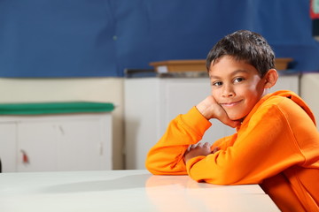 Schoolboy 10 wearing orange hoodie resting on classroom desk