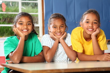 Three happy young school girls leaning on desk in class